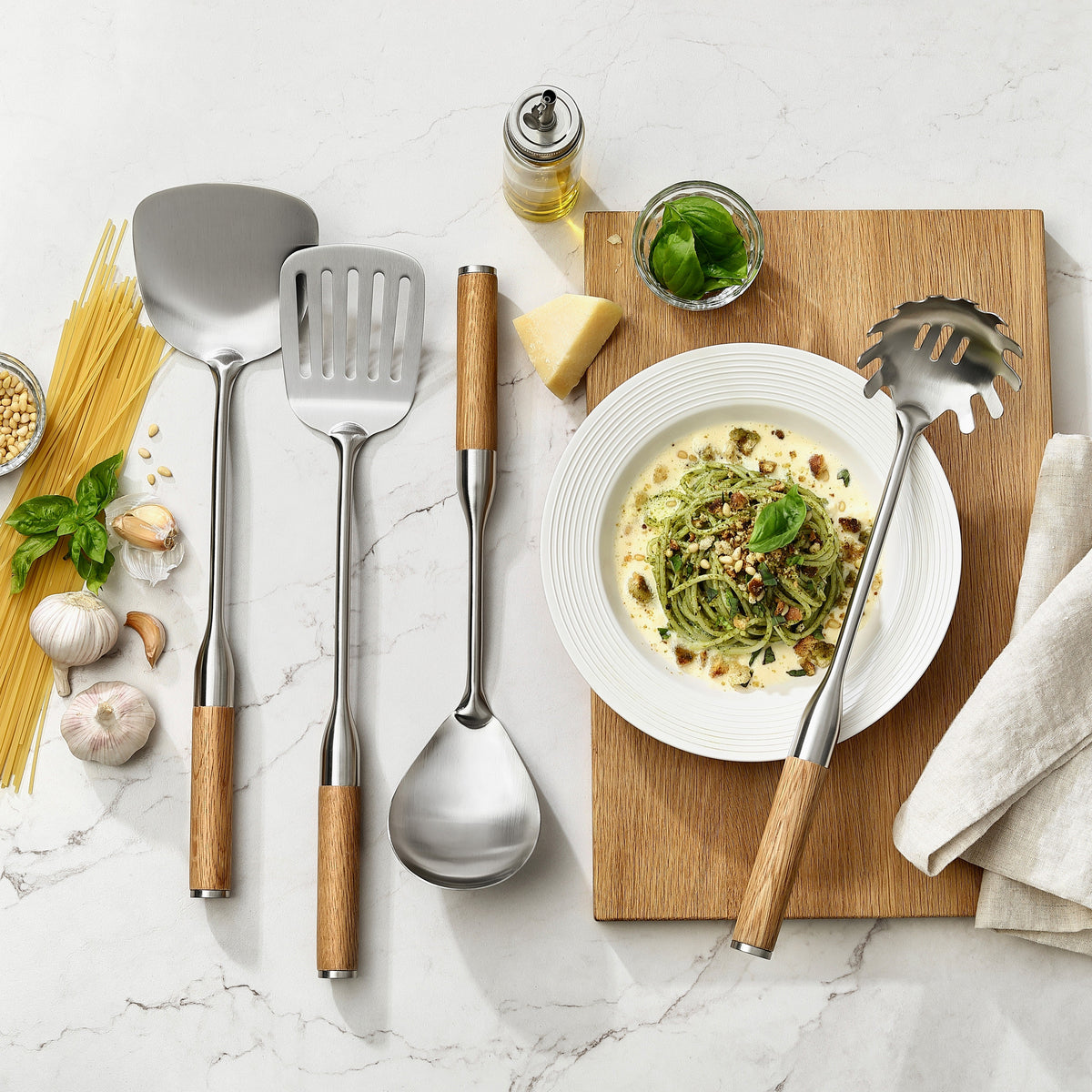 Pastaslev, stekspadar och serveringssked med handtag i ek på och bredvid en tallrik pasta med pesto