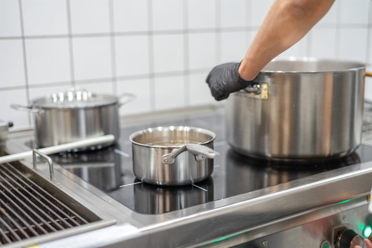Grytor och en kastrull i rostfritt stål på en induktionshäll i ett restaurangkök