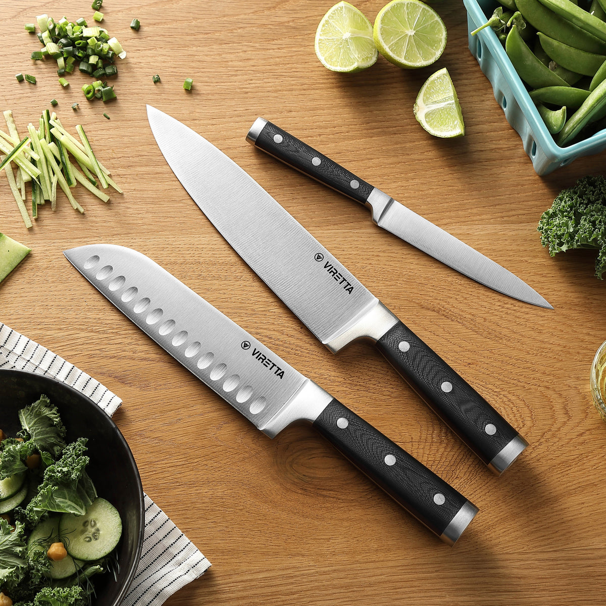 Classic santokukniv, kockkniv och universalkniv på ett träbord med limefrukter och grönt