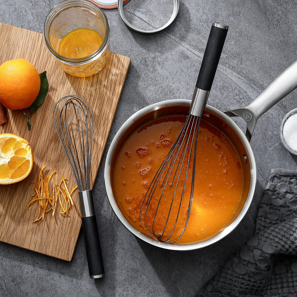 Två av Trio-setets vispar med handtag i G-10 – den ena i en kastrull med sås