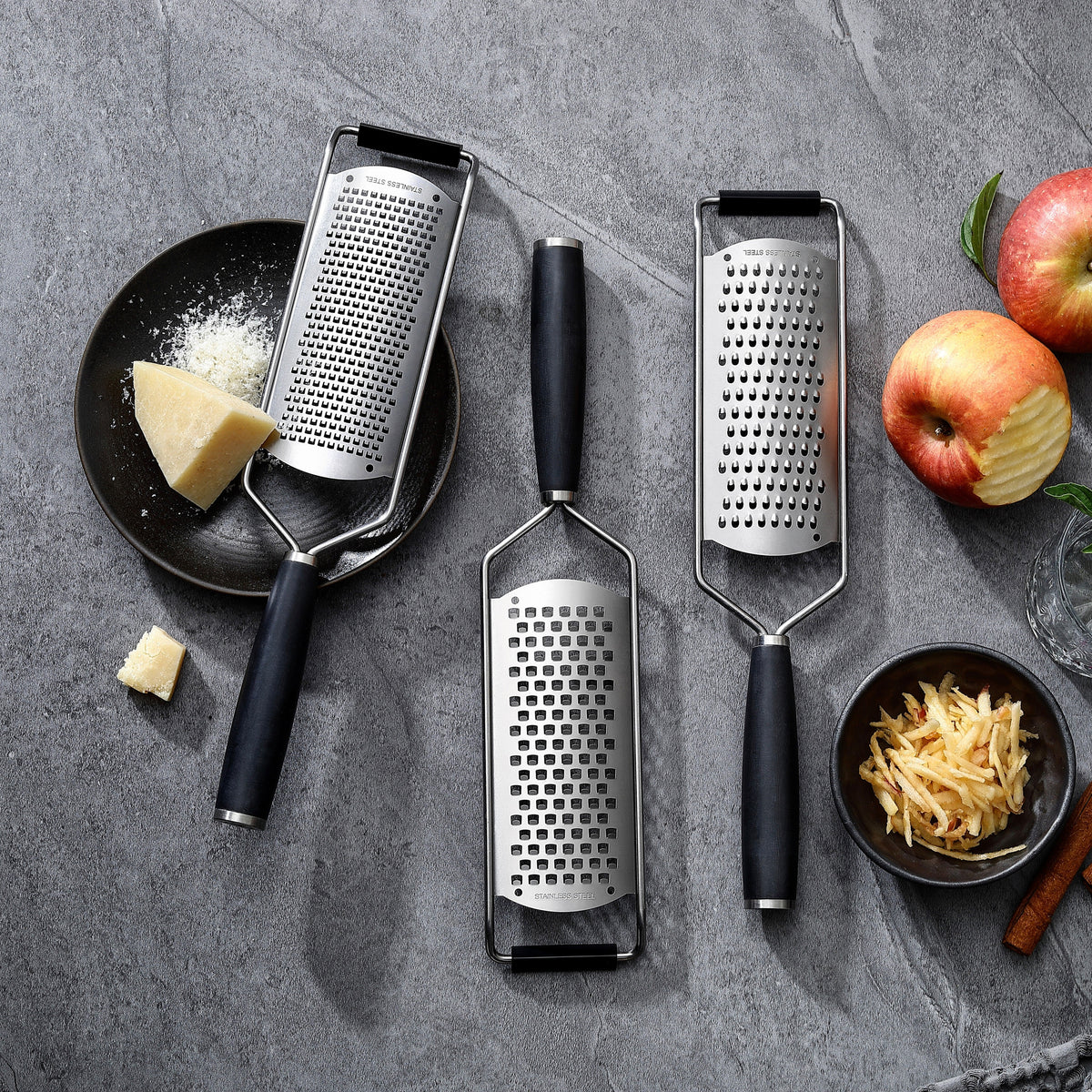 Fint, medium och grovt rivjärn med handtag i G-10 bredvid parmesan och äpplen