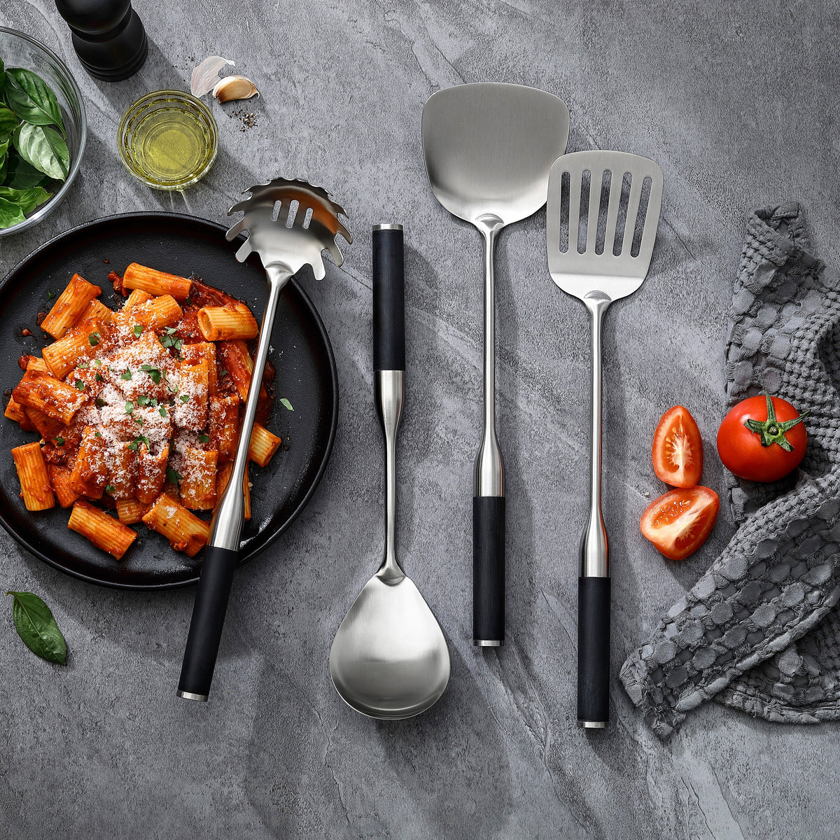 Setets fyra redskap med handtag i G-10 på och bredvid en tallrik rigatoni med tomatsås