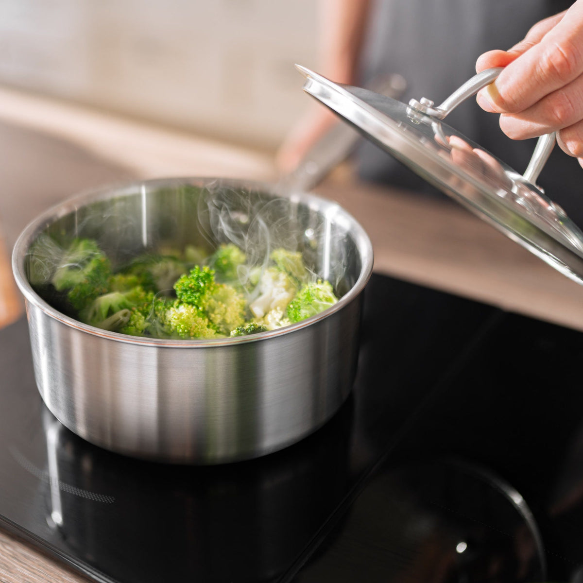 Broccoli ångkokas i en kastrull Ø20 cm i 5-Ply rostfritt stål på en induktionshäll, medan glaslocket lyfts av