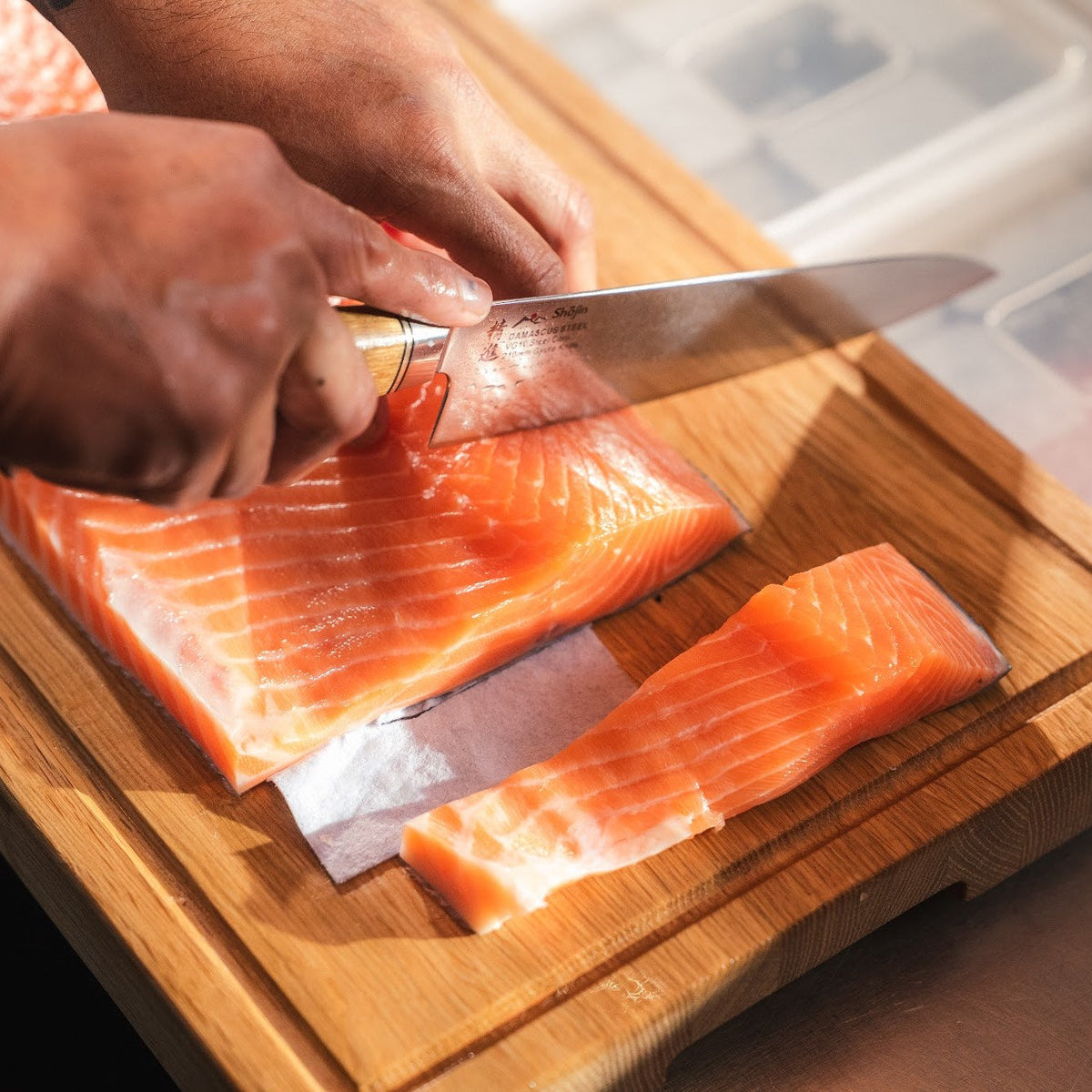 Lax skärs i portionsbitar med en Shōjin Kaku gyuto med ekskaft på en skärbräda i ek
