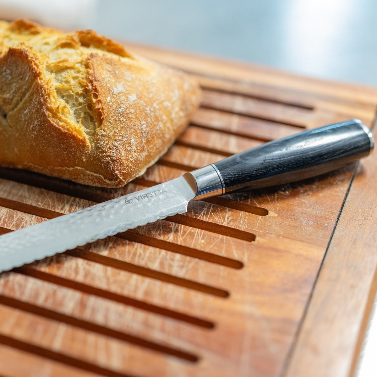 Shōjin Taru brödkniv med hamrat blad bredvid ett surdegsbröd på en brödbräda