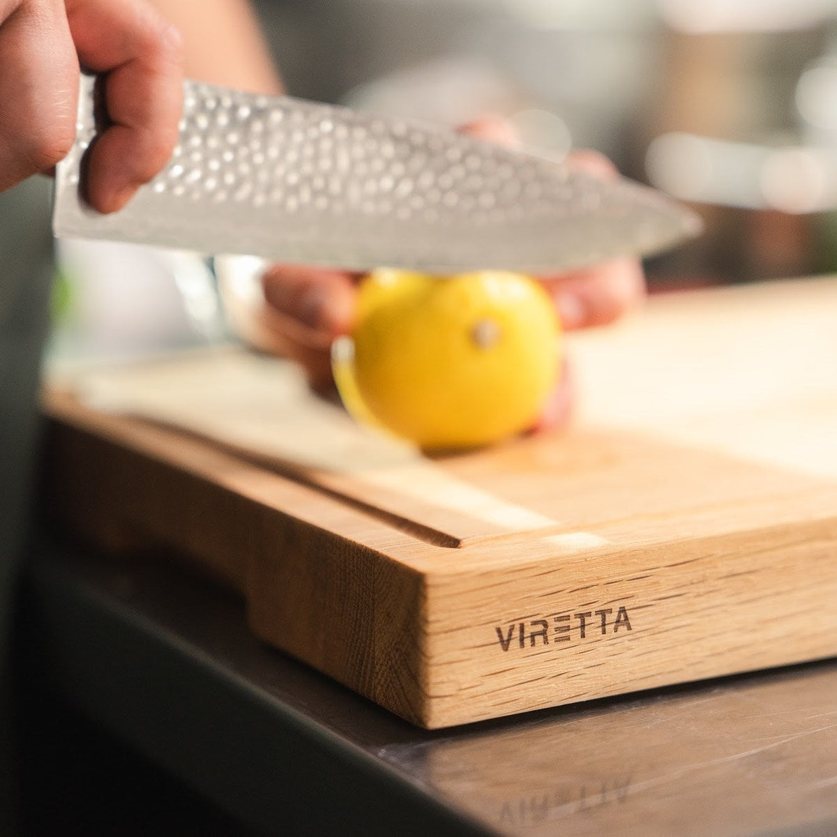 En citron skärs med en Shōjin Taru kockkniv på en skärbräda i ek med saftränna