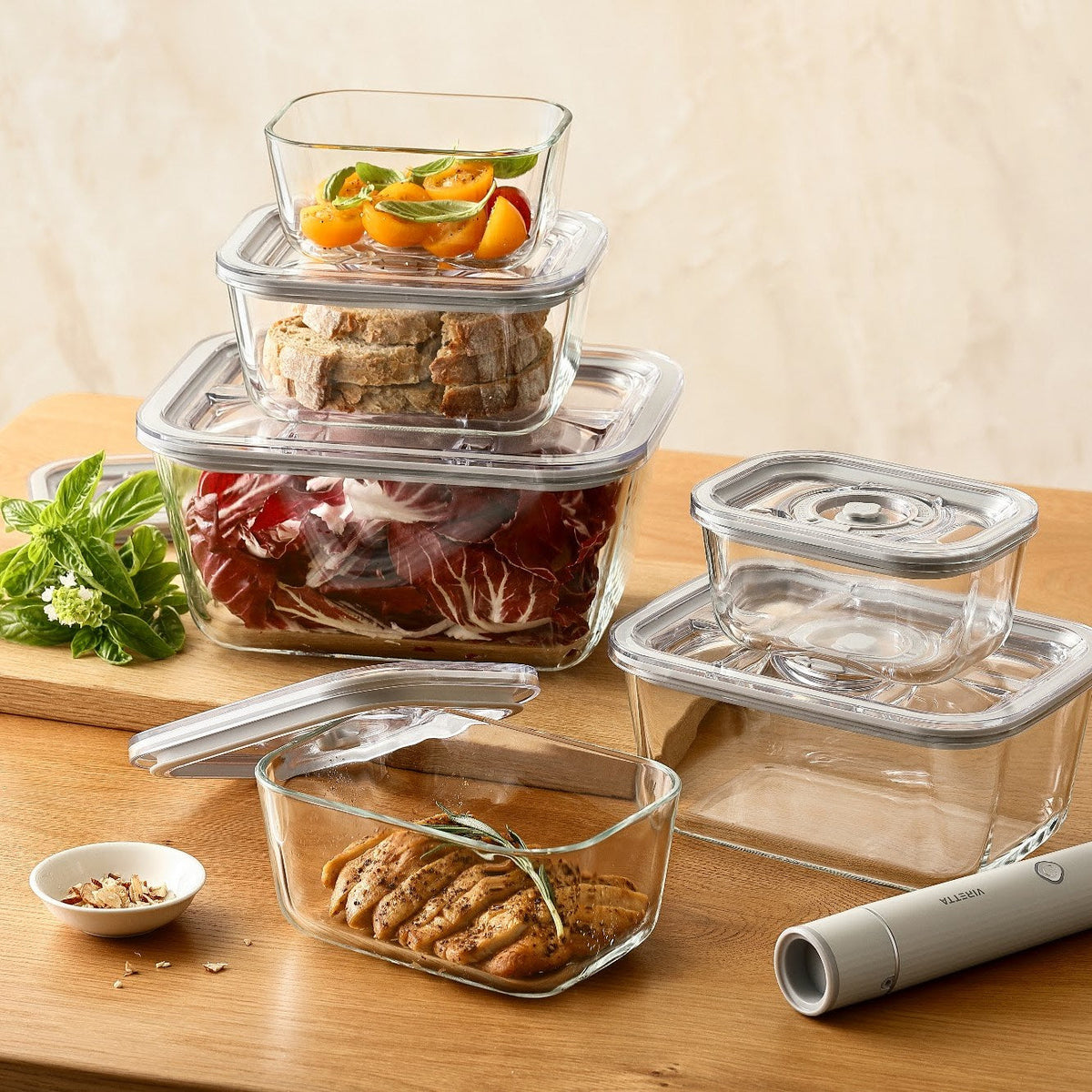 Vakuumbehållare i glas med tomater, bröd, sallad och kyckling på ett matbord