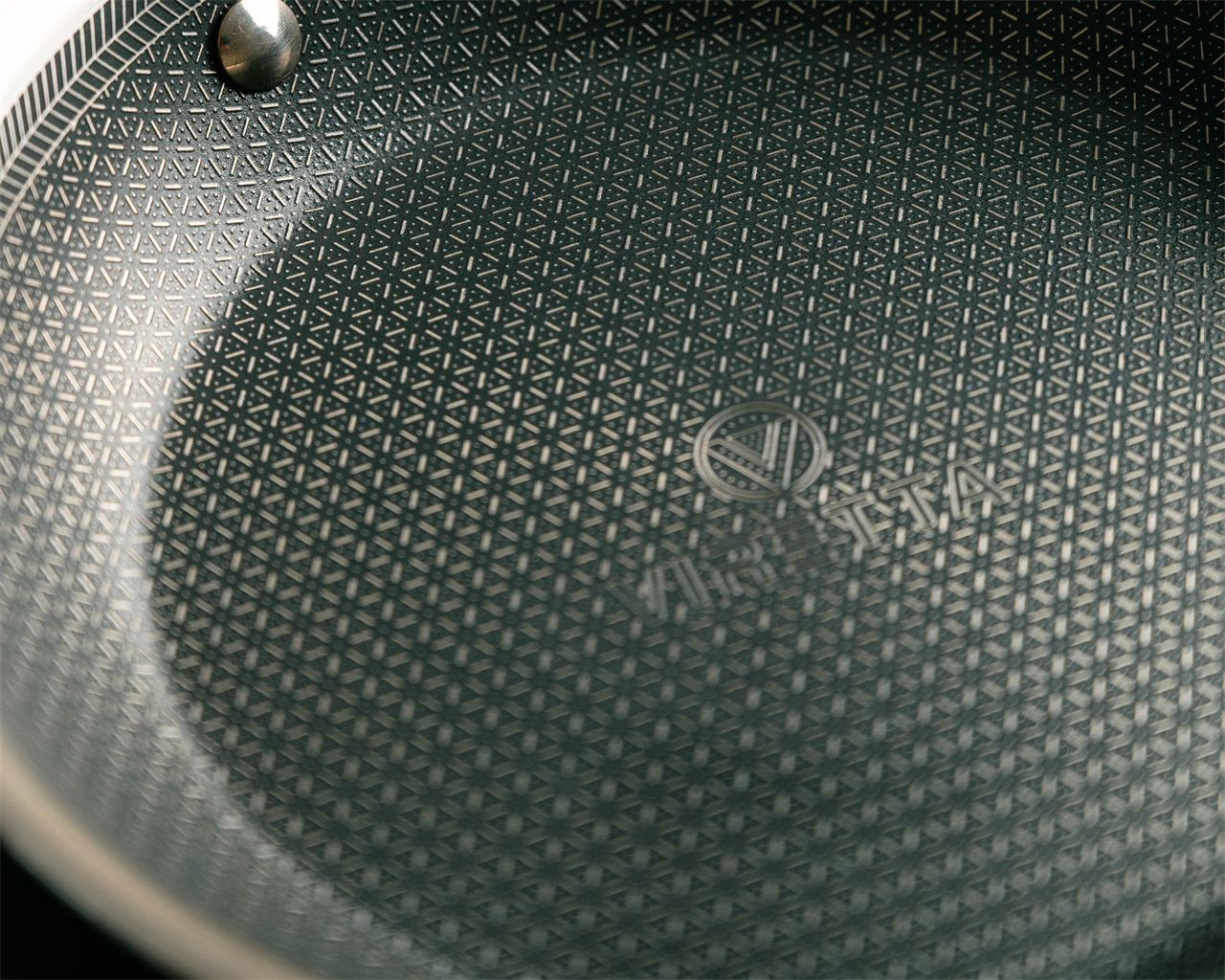 Stekytan på en Hybrid-panna i närbild: ett mönster av stål över den mörka beläggningen, med Viretta-logotypen i mitten