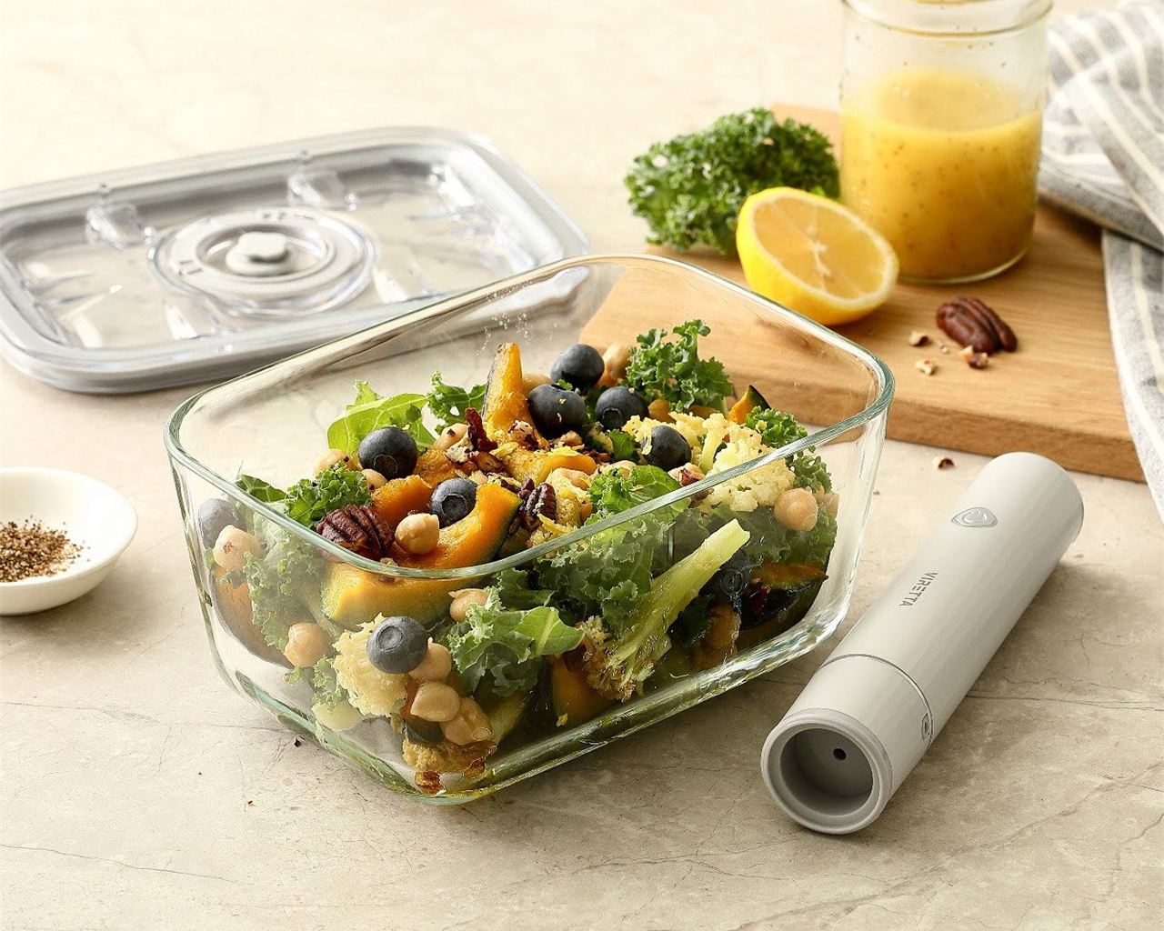 En vakuumbehållare i glas med sallad; locket och den elektriska vakuumpumpen ligger bredvid