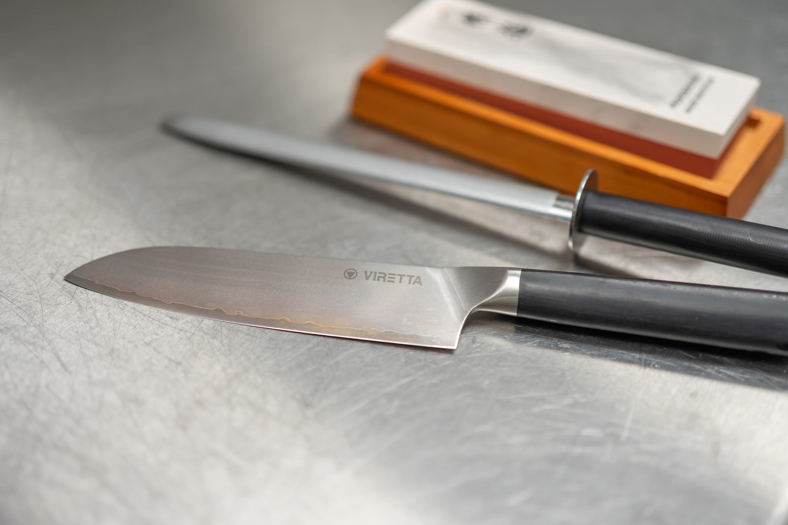 En santoku, ett skärpstål och en slipsten på en stålbänk i köket på Bolo