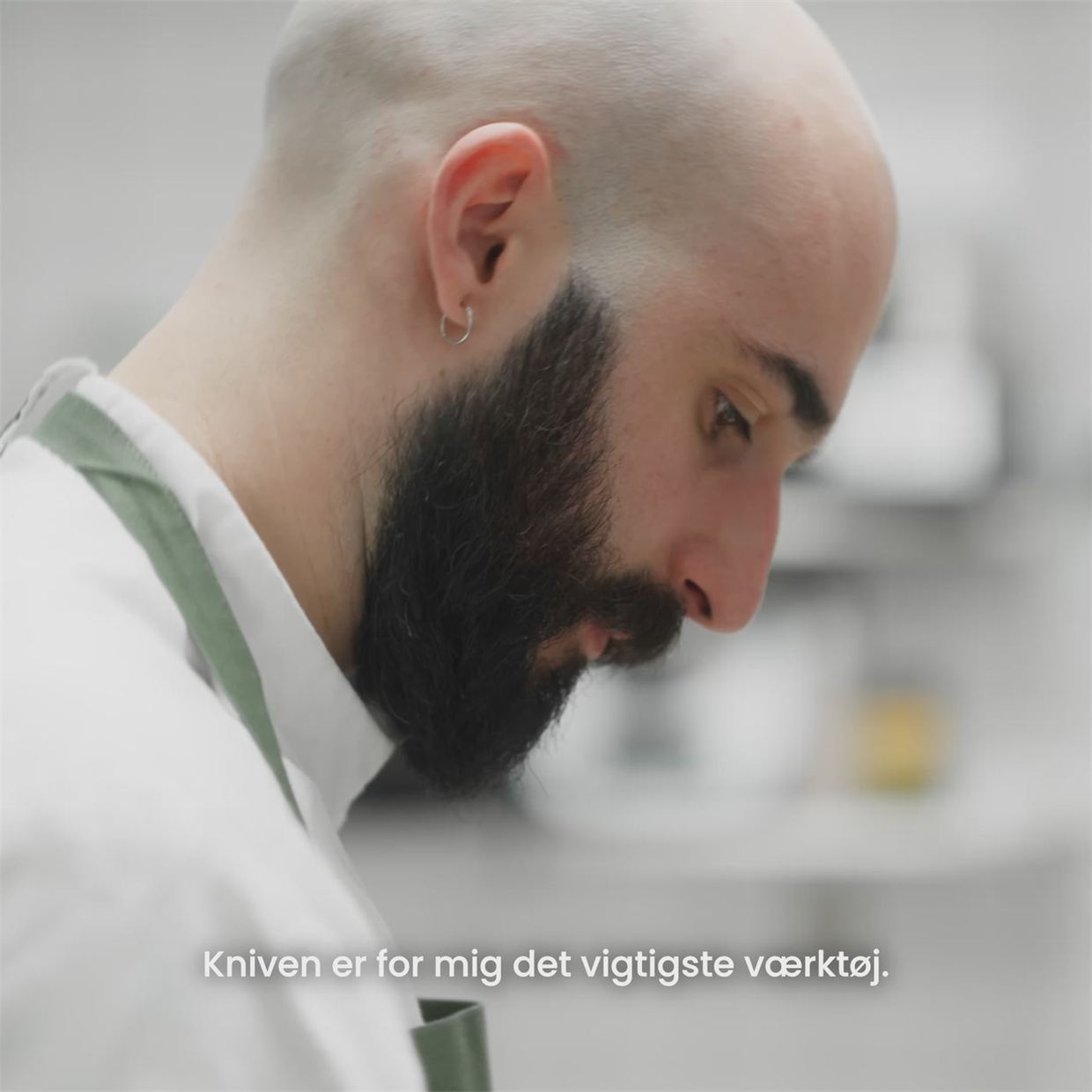 Santiago i vit kockrock och grönt förkläde böjer sig över arbetet i köket på Bolo