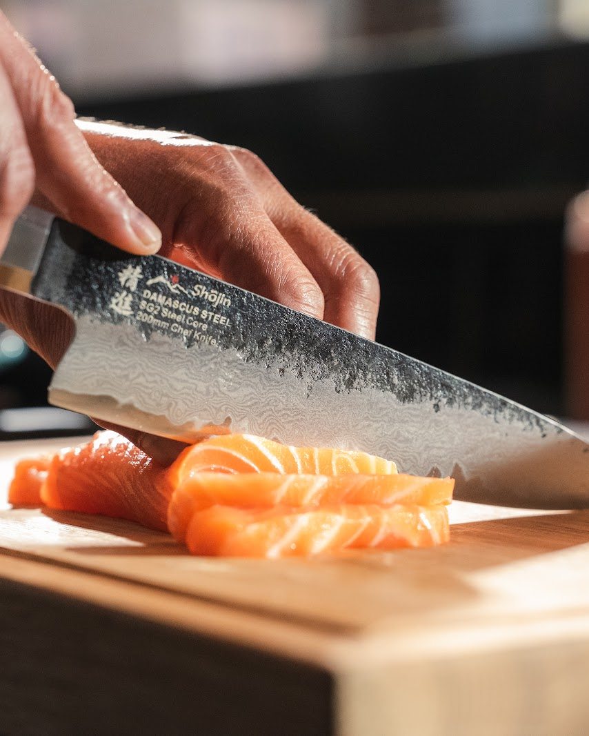 En kniv med hamrat blad skär lax i skivor på en skärbräda