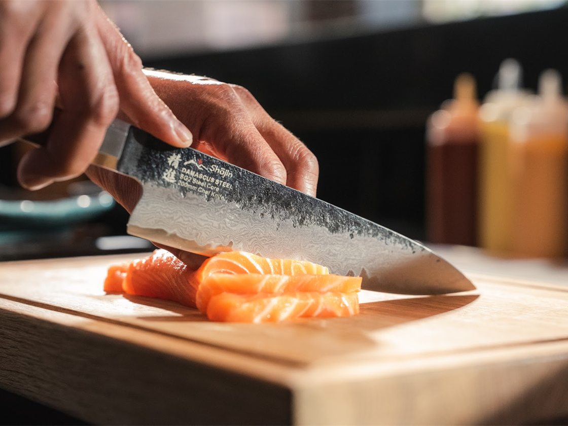 En kniv med hamrat blad skär lax i skivor på en skärbräda