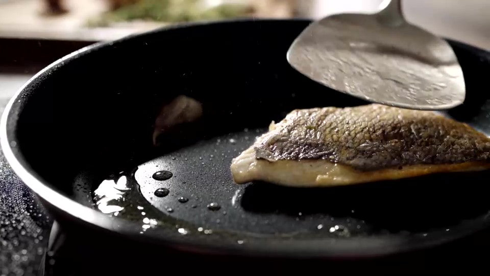 En bit fisk läggs i en panna i Titanium Plasma och vänds med en stekspade i metall